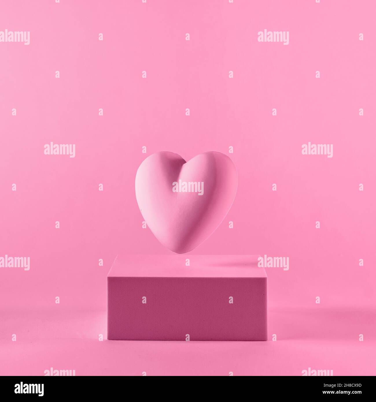 Studio gros plan d'une forme de coeur 3d flottant au-dessus d'un podium rectangulaire sur fond blanc rose pour l'espace de copie comme symbole pour dating ou cardiolog Banque D'Images