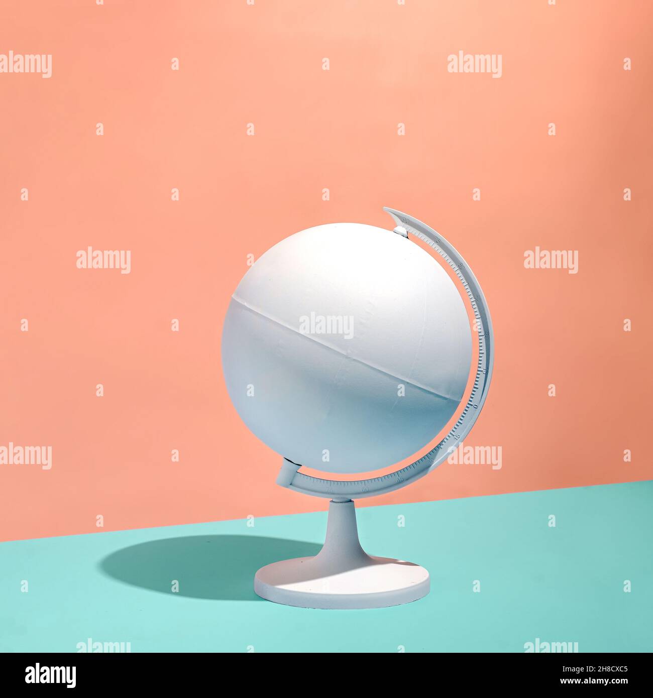 Globe blanc vierge sur un piédestal qui projette une ombre sur un fond abricot bicolore ou orange et vert avec un espace de copie au format carré Banque D'Images