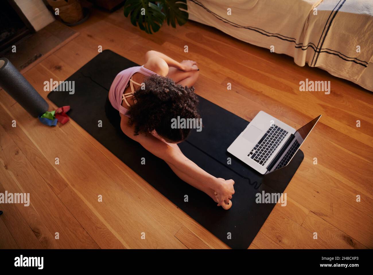 Bonne jeune femme multiculturelle suivant un didacticiel sur son ordinateur portable à la maison dans son salon moderne Banque D'Images