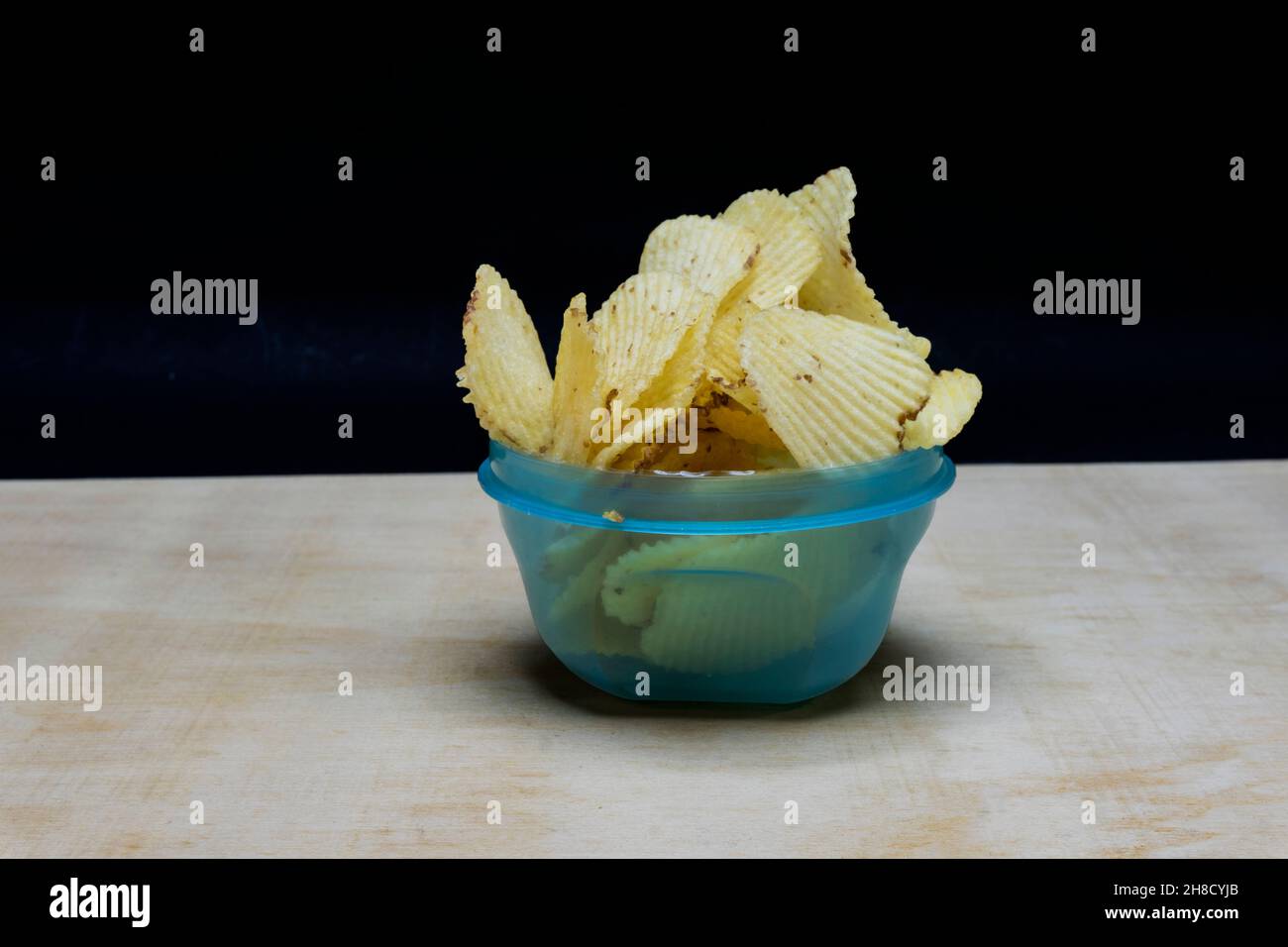 Copeaux de pommes de terre salés dans un bol de cyan clair sur la table, isolés sur fond noir, tas de copeaux de pommes de terre Banque D'Images