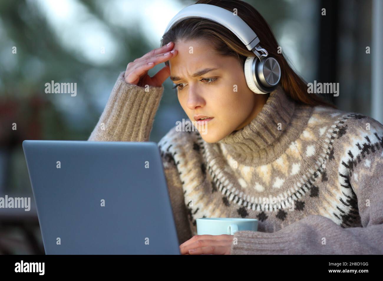 Femme frustrée en hiver regardant des médias sur un ordinateur portable sur une terrasse Banque D'Images