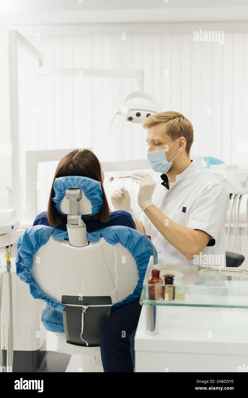 Un dentiste de sexe caucasien examine les dents d'une jeune femme à la clinique dentaire. Un médecin sondant les dents avec un instrument dentaire en utilisant un explorer recherchez les problèmes de traitement et de vérification des cavités Banque D'Images