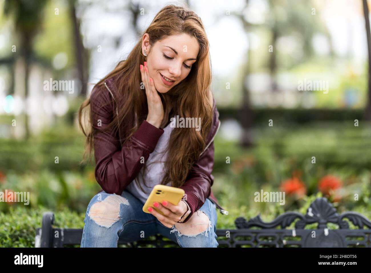 Jeune fille écrivant un message avec son smartphone assis sur un banc dans le format de parc avec l'espace de copie de près Banque D'Images