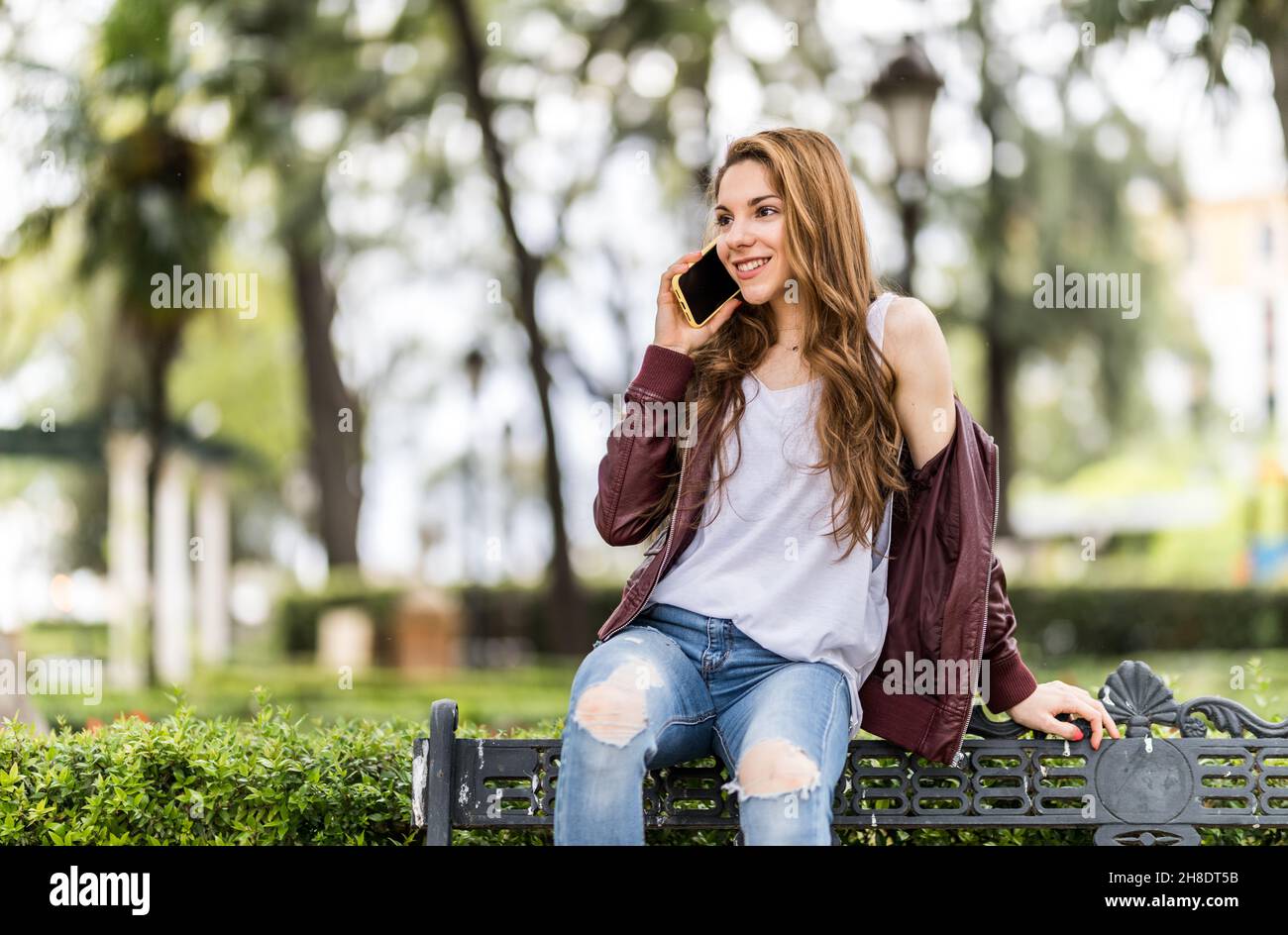 Jeune fille souriant avec son smartphone assis sur un banc au format parc avec espace de copie de près Banque D'Images