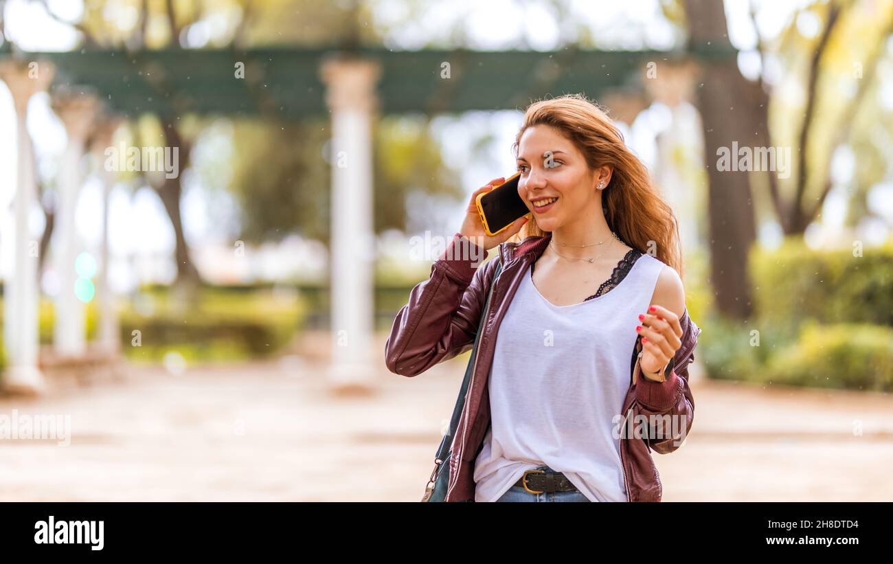 Une adolescente souriante et naturelle parle avec son smartphone dans le parc Banque D'Images