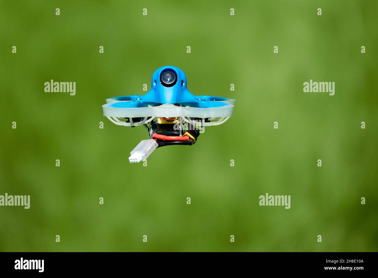 Petit bleu Drone également quad de course, avec la gondole de protection en blanc avec un fond flou de vert.Allemagne. Banque D'Images