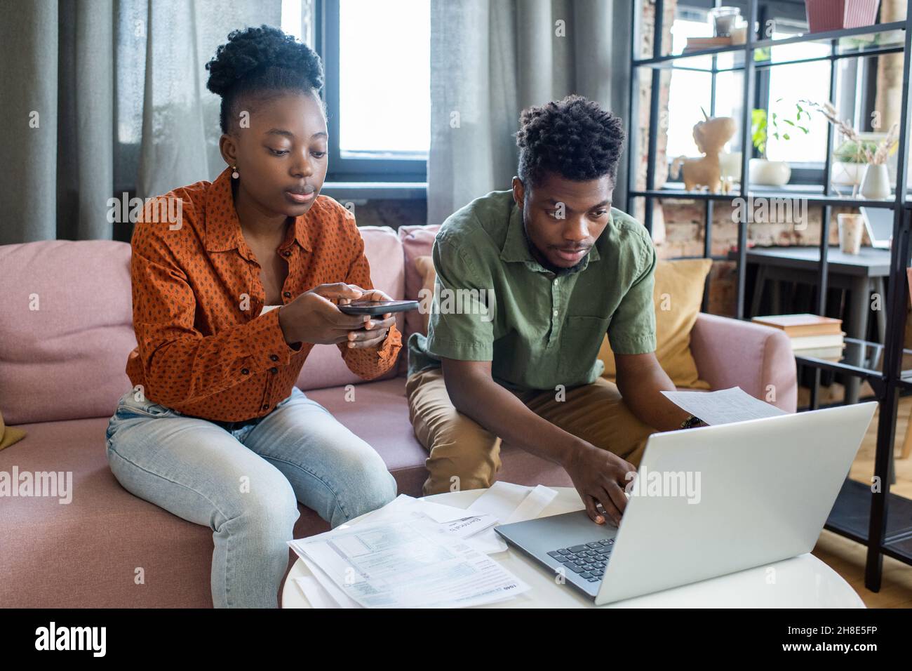 Un jeune couple afro-américain en costume décontracté utilisant des appareils modernes tout en préparant des dossiers fiscaux Banque D'Images