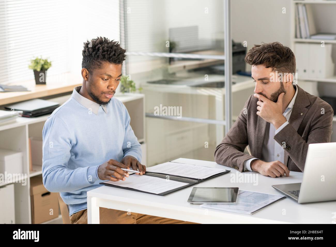 Jeune homme d'affaires afro-américain concentré lisant le contrat avant du signer lors d'une réunion avec un partenaire d'affaires ou un avocat en fonction Banque D'Images