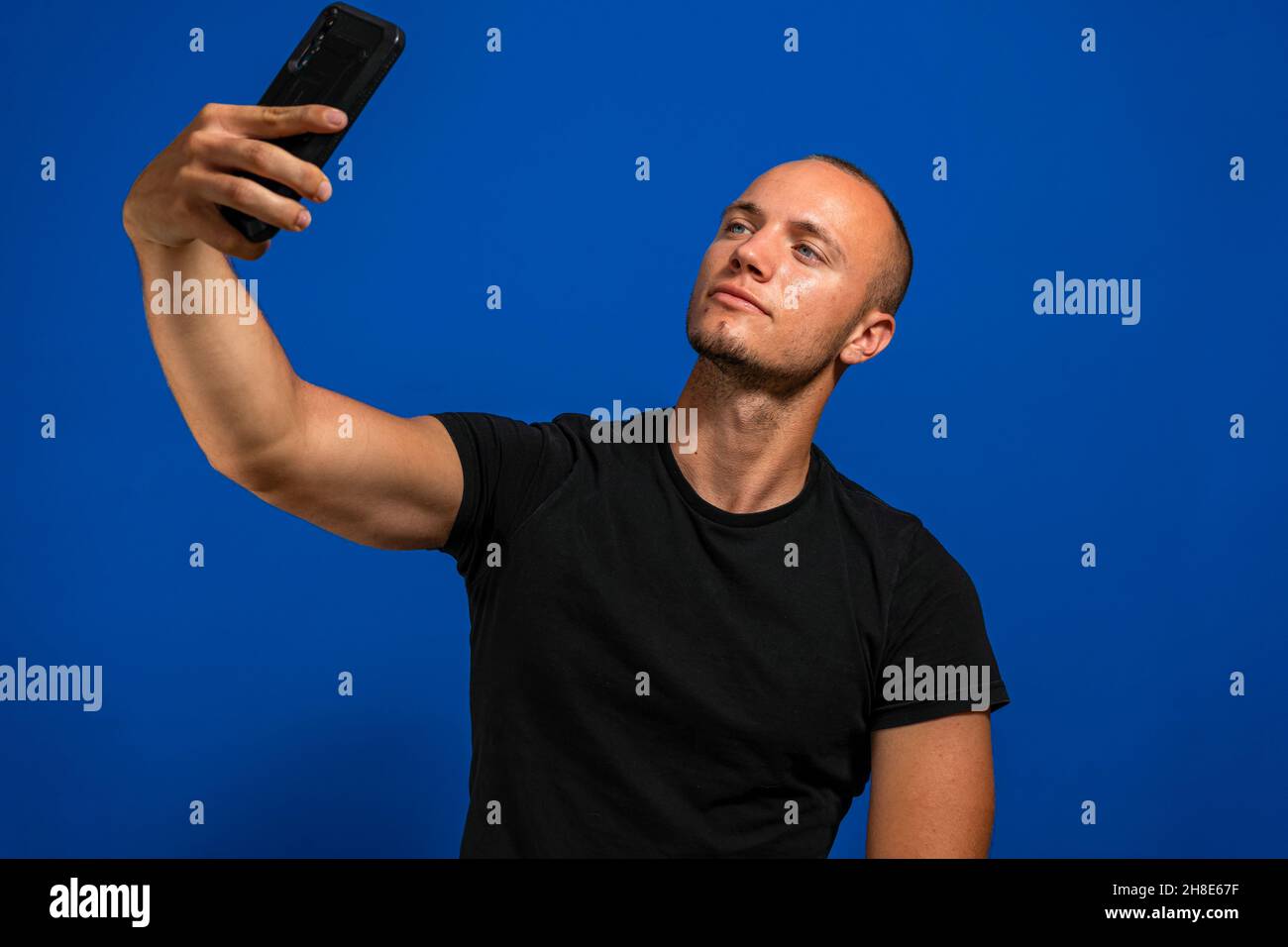 Beau jeune homme caucasien avec des cheveux blonds et des yeux bleus prenant un selfie isolé sur fond bleu studio Banque D'Images