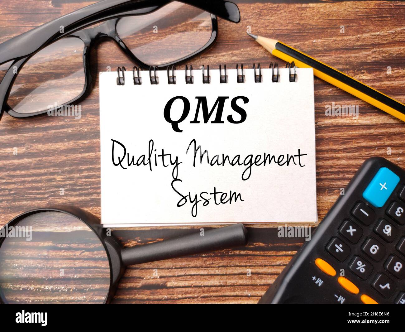 Lunettes, calculatrice, crayon et bloc-notes avec texte QMS système de gestion de la qualité sur une table en bois Banque D'Images