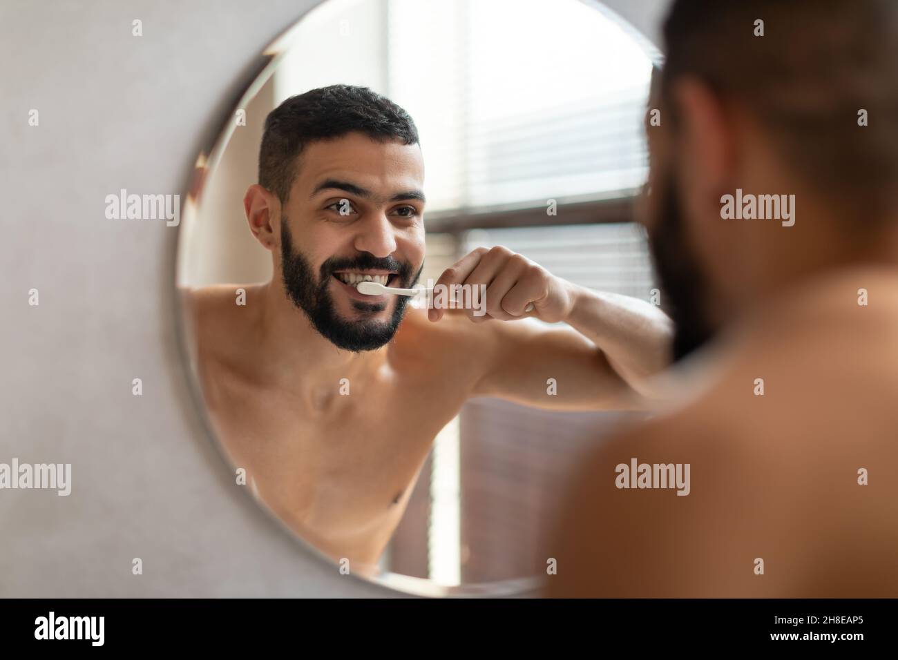 Beau jeune homme arabe utilisant la brosse à dents dans la salle de bains Banque D'Images