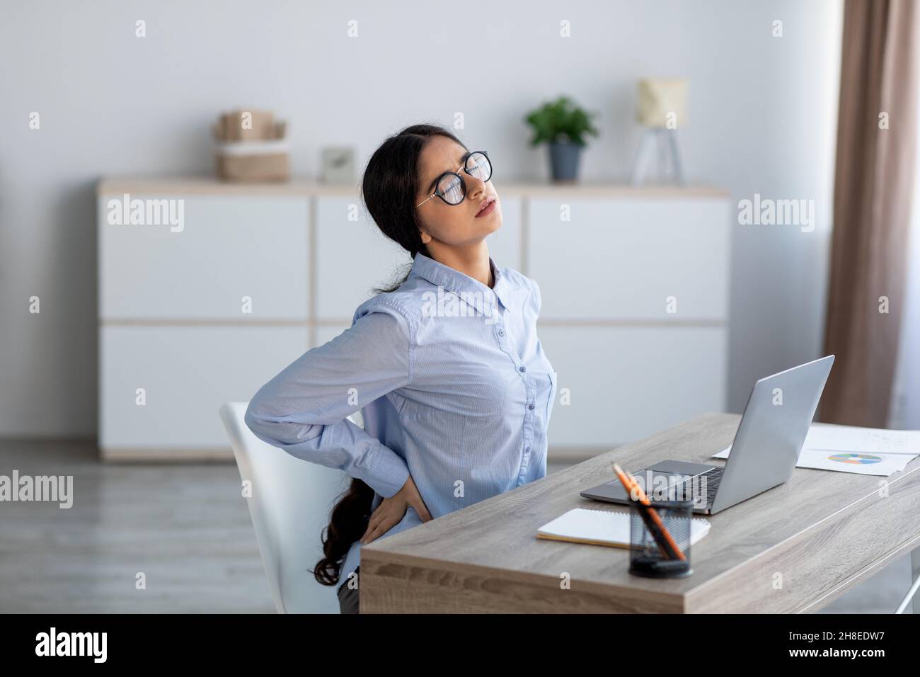 Fatiguée bouleversée jeune femme d'affaires indienne souffrant de douleurs dorsales, spasme musculaire au travail avec ordinateur portable Banque D'Images