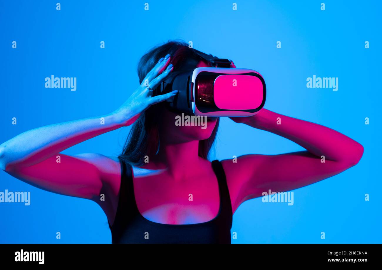 Fille gaie avec les mains vers le haut portant les lunettes de réalité virtuelle et jouant à un jeu dans la lumière de néon.Concept technologique futur.Métaverse. Banque D'Images