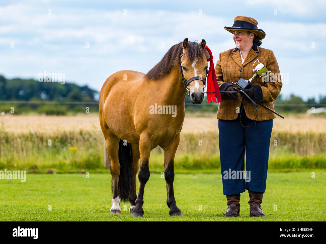 Fière femme tenant le trophée du gagnant avec le cheval portant la rosette de prix à l'événement équestre d'été, East Lothian, Écosse, Royaume-Uni Banque D'Images