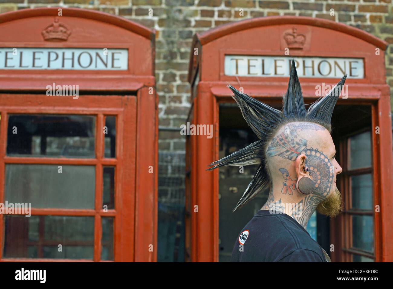 Punk avec la coiffure mohawk devant la boîte téléphonique rouge Banque D'Images
