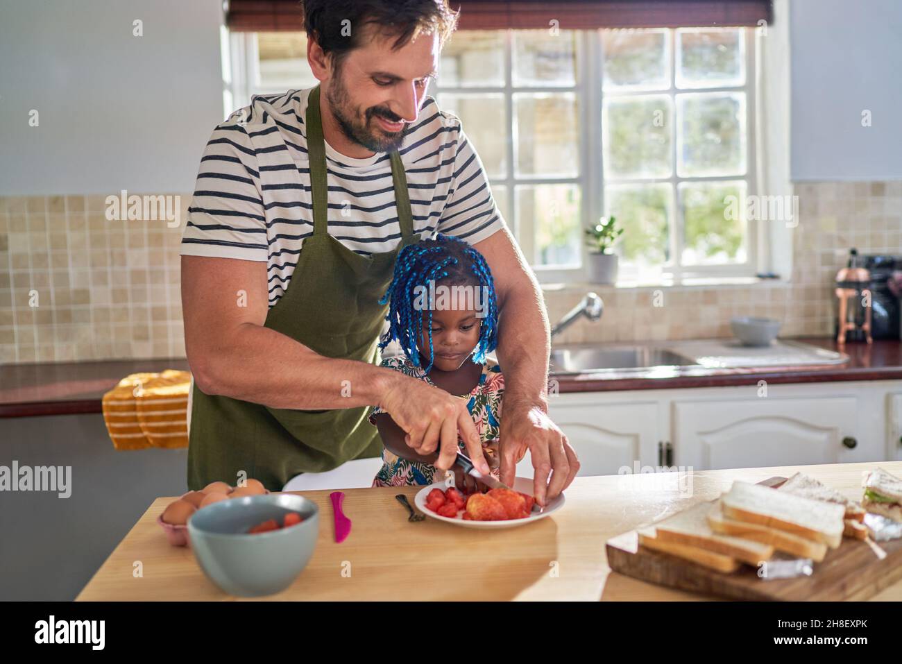 Père coupant des fruits pour petite fille dans la cuisine Banque D'Images