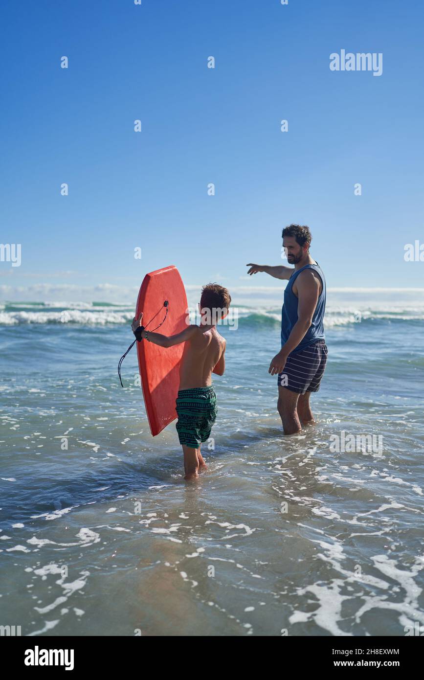 Père et fils avec planche à voile dans les vagues ensoleillées de l'océan Banque D'Images