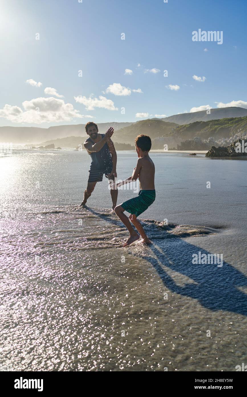 Un père amusant éclabousse son fils sur une plage ensoleillée d'été Banque D'Images