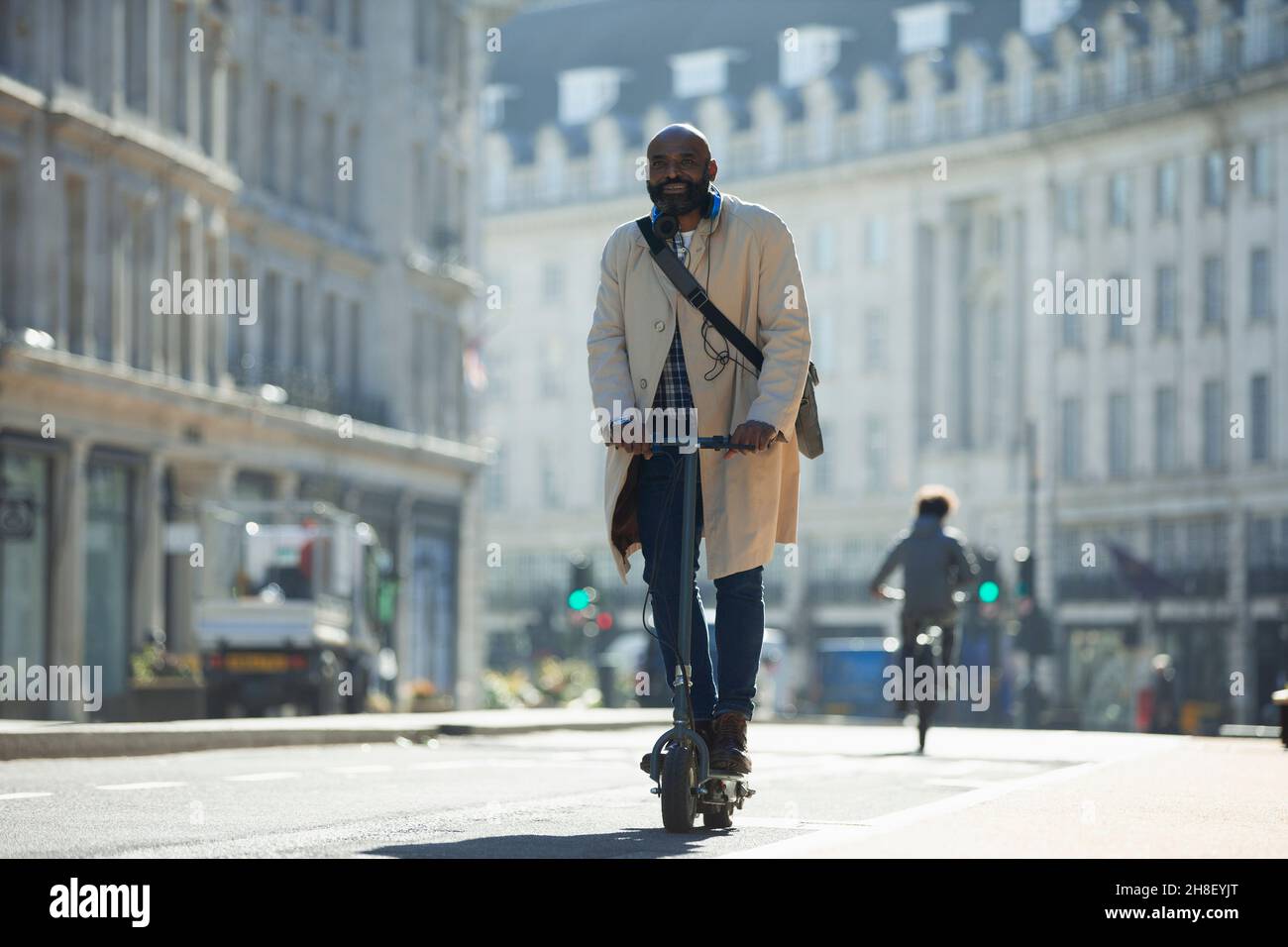 Homme d'affaires à bord d'un scooter électrique sur une rue ensoleillée de la ville Banque D'Images