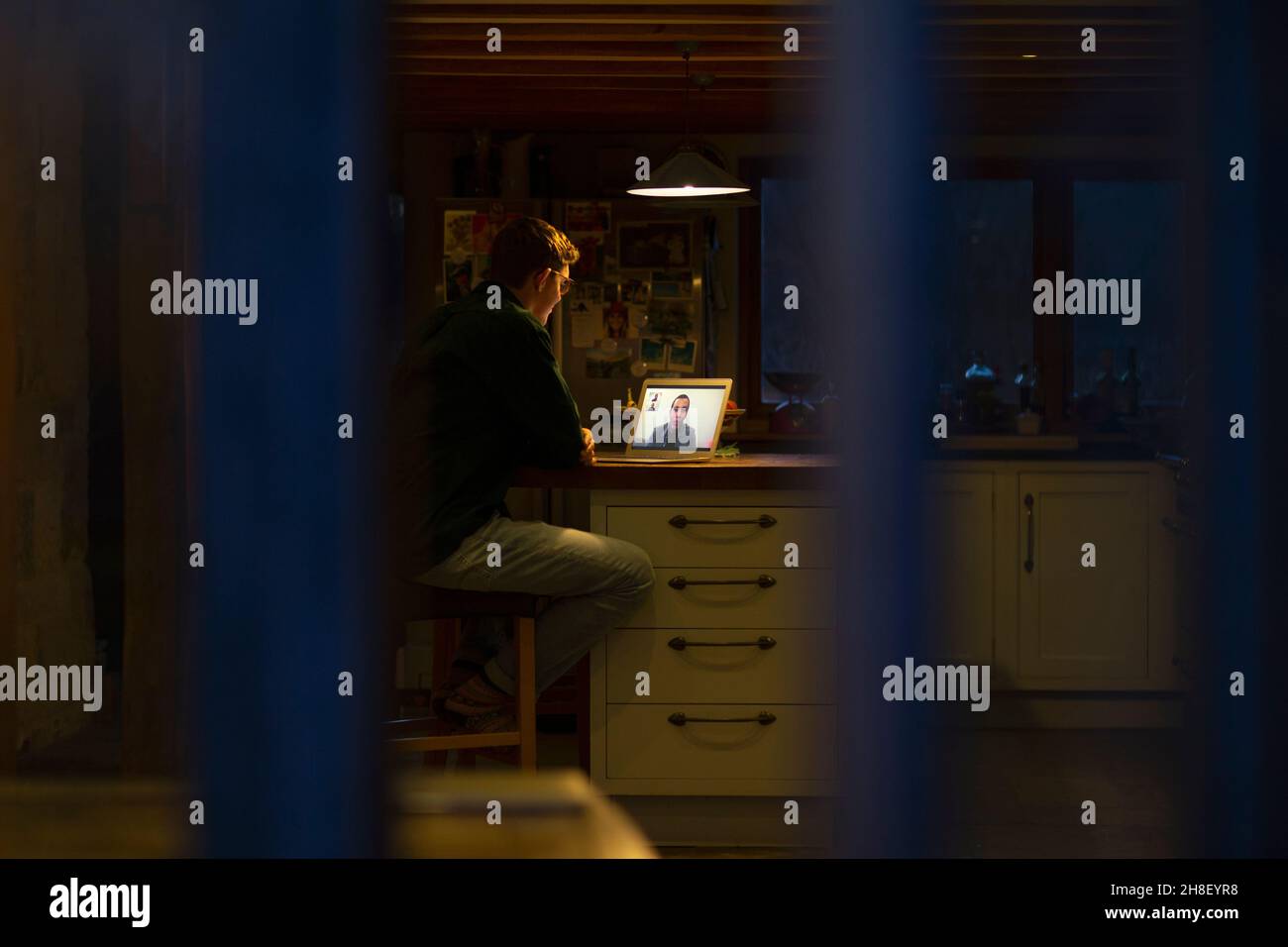 Homme travaillant tard dans la visioconférence sur un ordinateur portable dans une cuisine sombre Banque D'Images