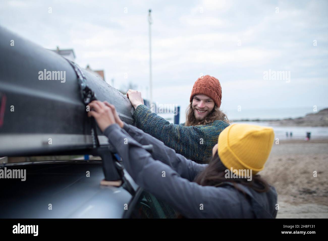 Un jeune couple heureux qui retire le canoë du haut de la voiture sur la plage Banque D'Images