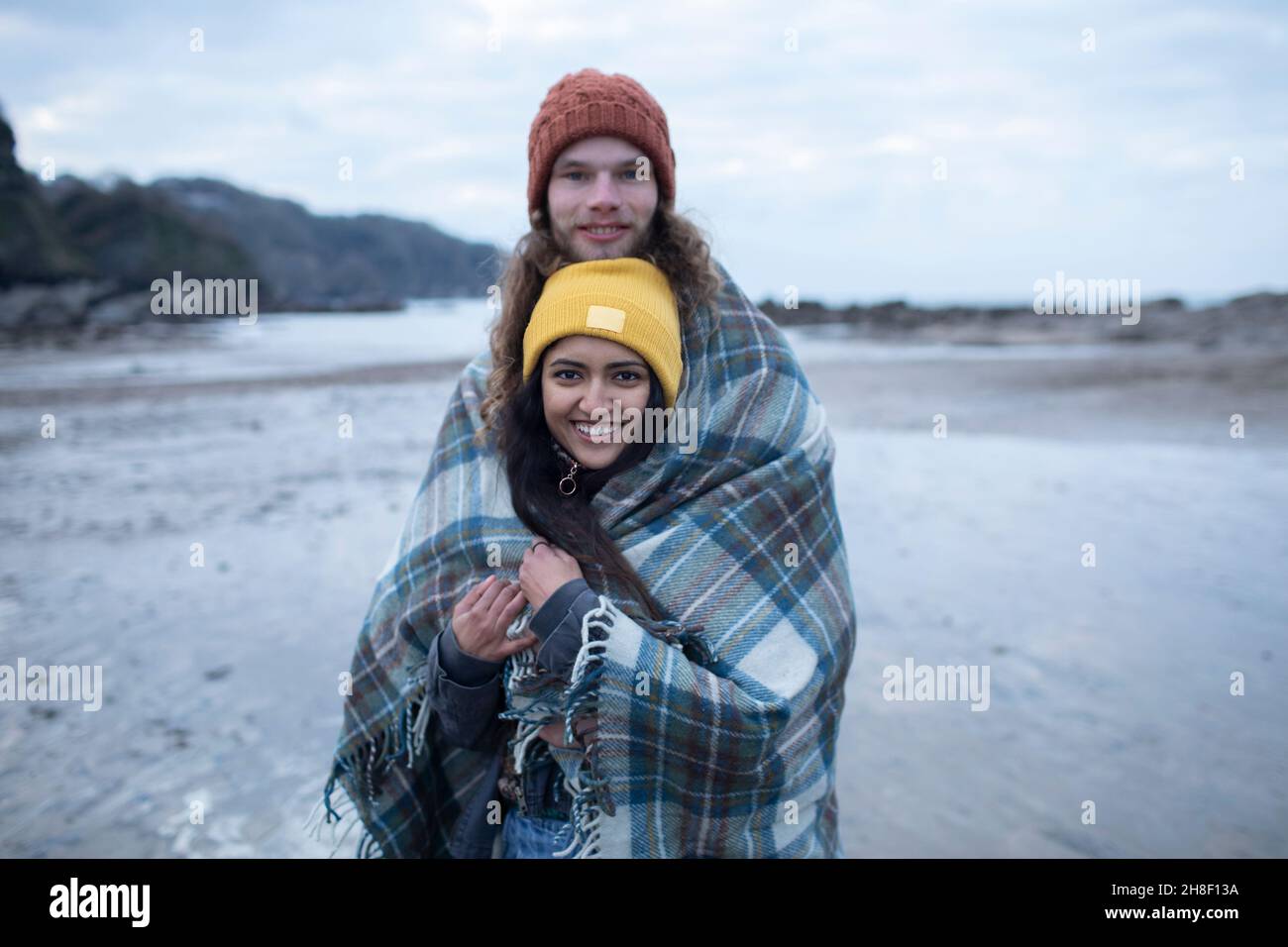 Portrait jeune couple heureux enveloppé dans une couverture sur une plage froide Banque D'Images