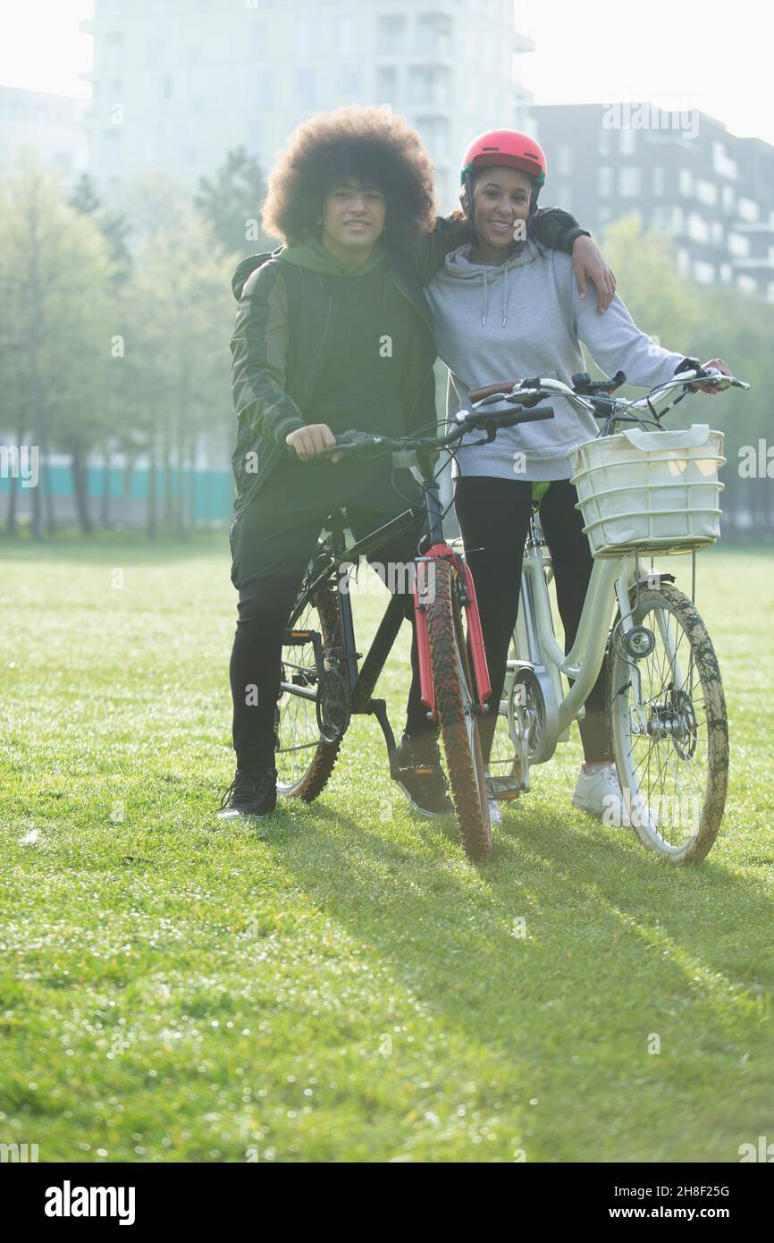 Portrait heureux couple d'adolescents sur des vélos dans l'herbe de parc urbain Banque D'Images Portrait heureux couple d'adolescents sur des vélos dans l'herbe de parc urbain Banque D'Images