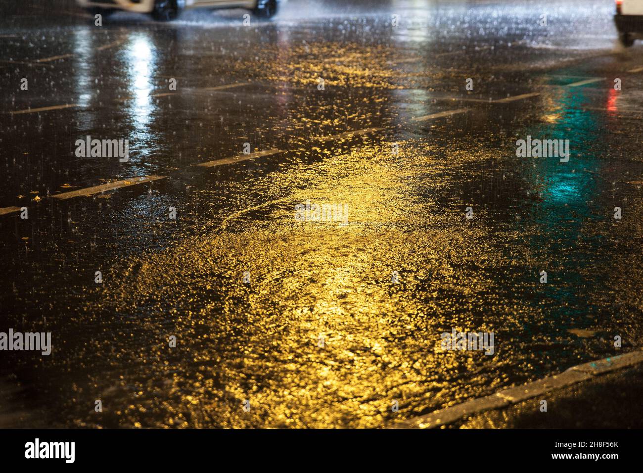 Photo d'une route humide dans un environnement urbain la nuit, avec des lumières urbaines en arrière-plan et des gouttes de pluie. Banque D'Images