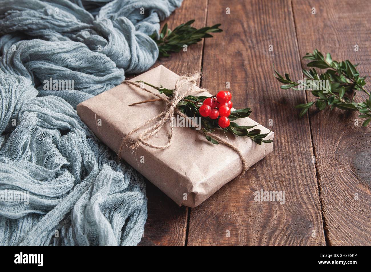 Boîte cadeau à côté de la nappe vintage grise et laisse des baies rouges sur une table en bois marron, composition festive sur fond naturel Banque D'Images
