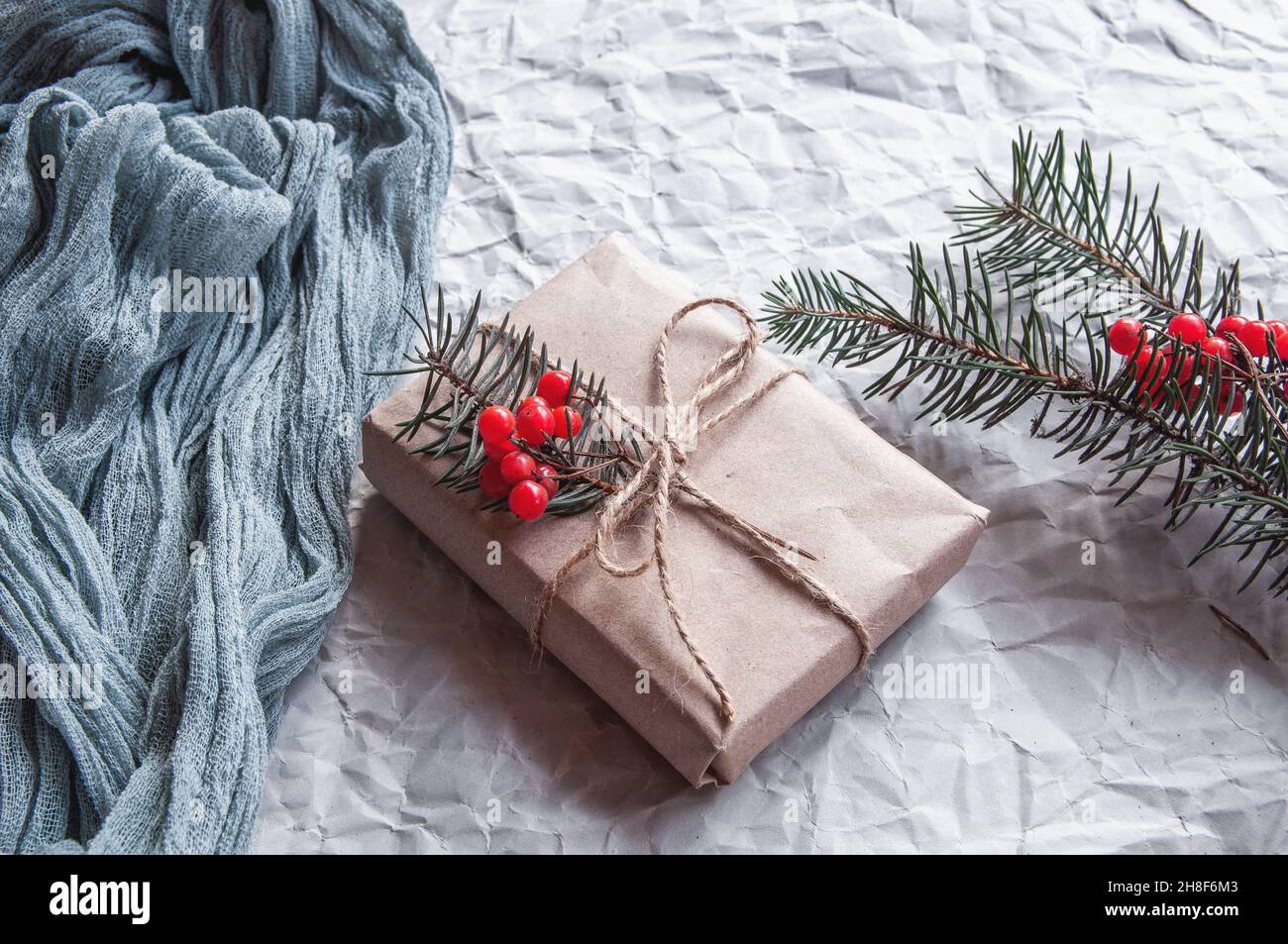 Boîte cadeau à côté de la nappe vintage gris et feuilles d'épinette avec baies rouges sur fond blanc, composition festive sur fond clair Banque D'Images