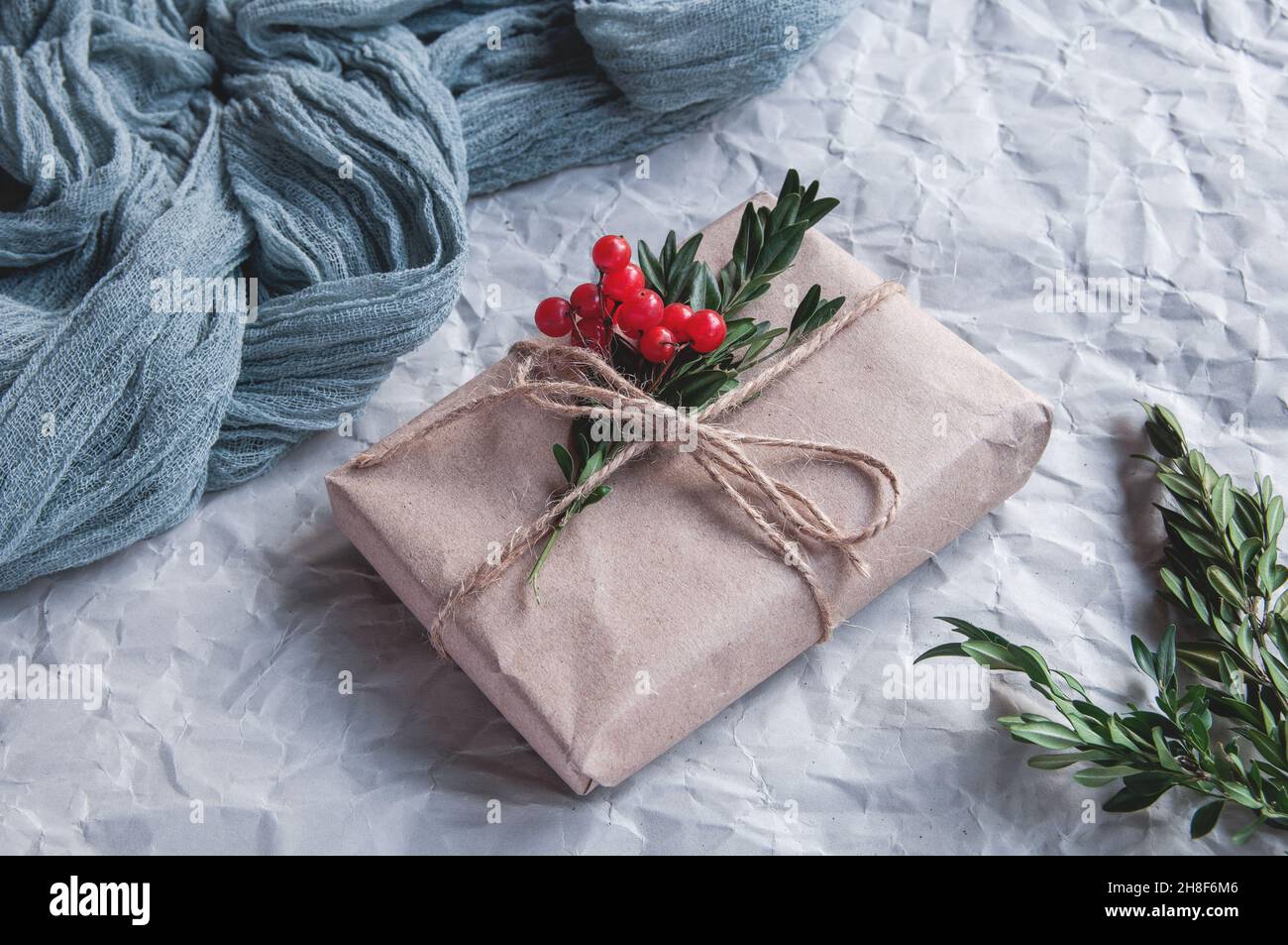 Boîte cadeau à côté de la nappe vintage gris et feuilles d'épinette avec baies rouges sur fond blanc, composition festive sur fond clair Banque D'Images