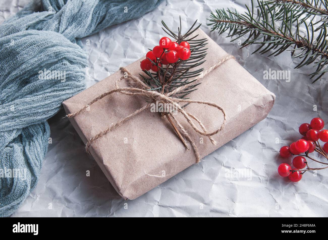 Boîte cadeau à côté de la nappe vintage gris et feuilles d'épinette avec baies rouges sur fond blanc, composition festive sur fond clair Banque D'Images
