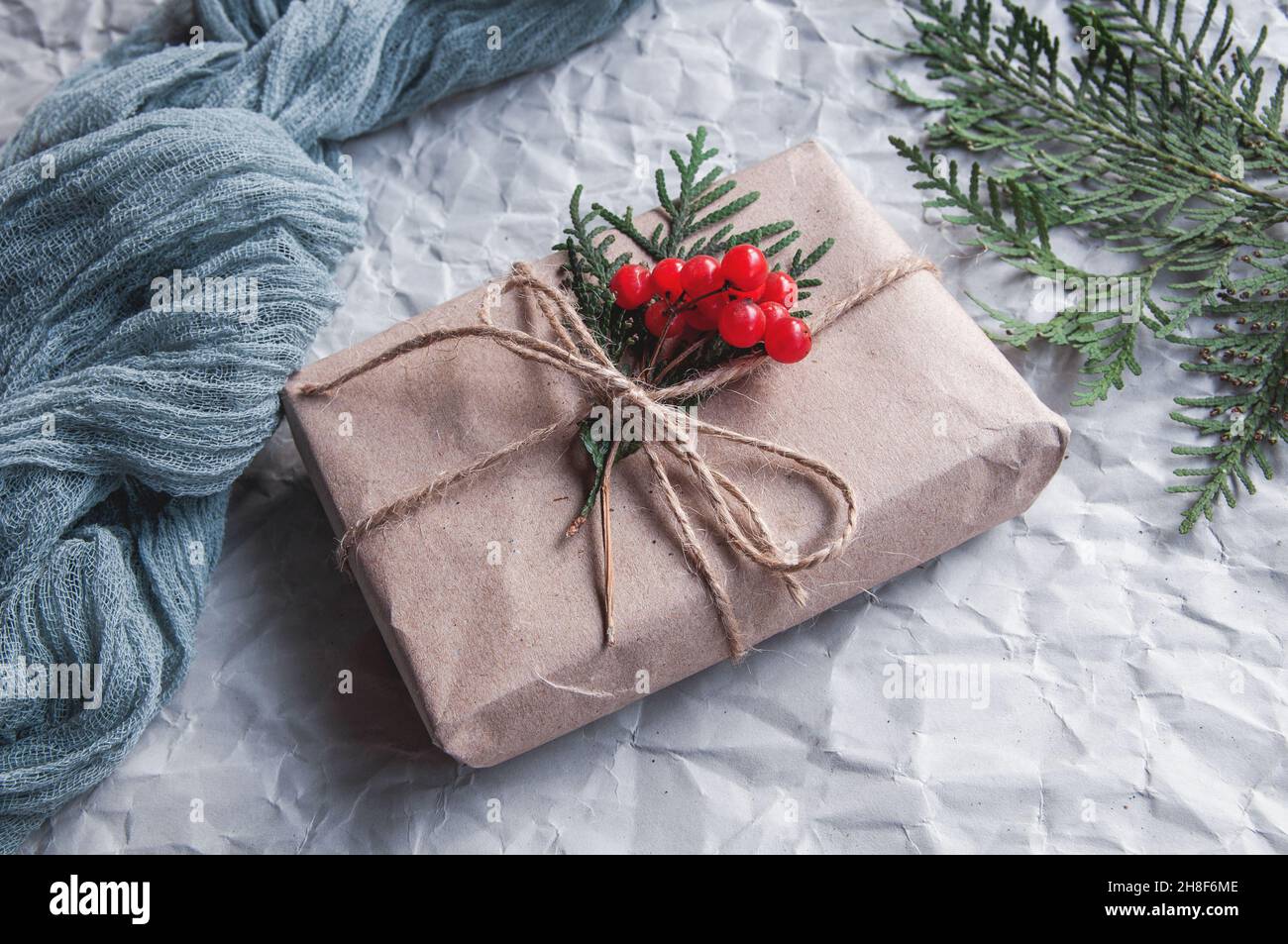 Boîte cadeau à côté de la nappe vintage gris et feuilles d'épinette avec baies rouges sur fond blanc, composition festive sur fond clair Banque D'Images