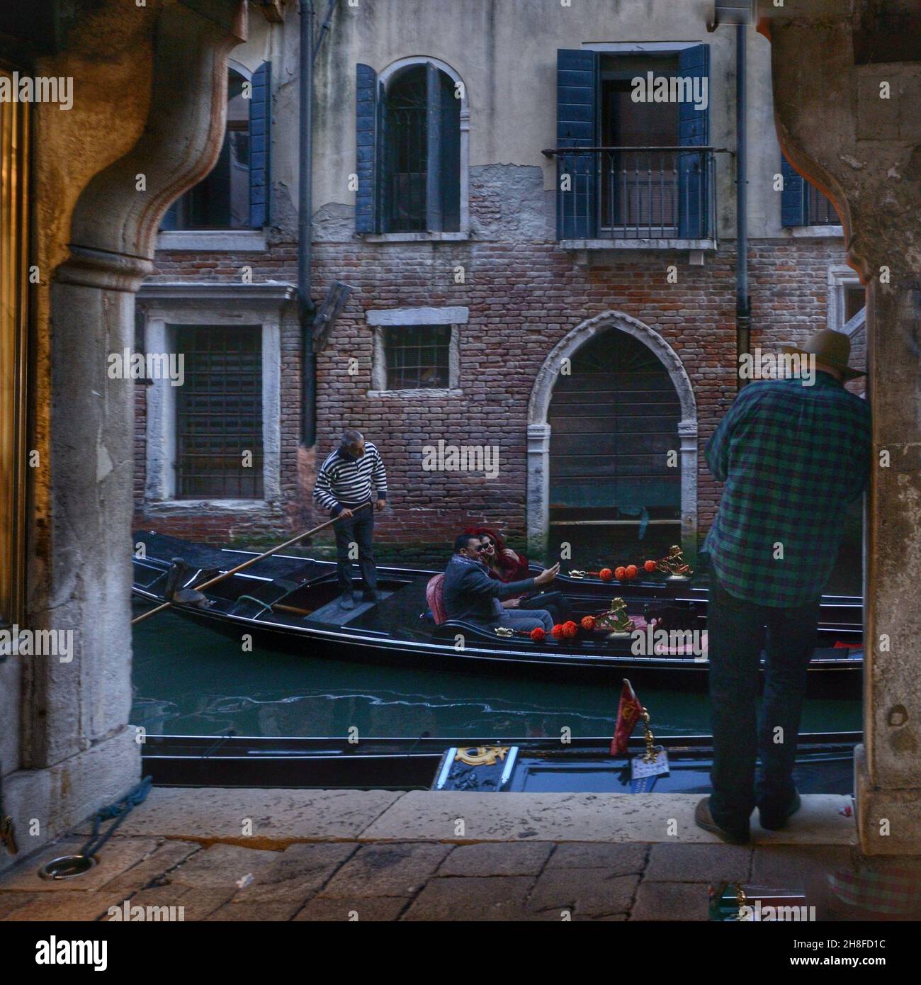 Vue sur une boutique vénitienne typique à proximité d'un canal au crépuscule.Un touriste prend une photo lorsqu'une gondole passe Banque D'Images