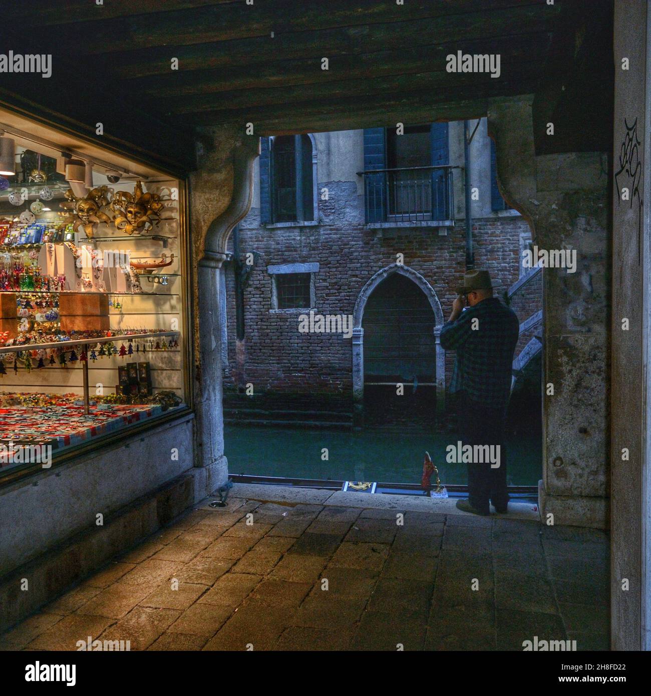 Vue sur une boutique vénitienne typique à proximité d'un canal au crépuscule.Un touriste prend une photo Banque D'Images
