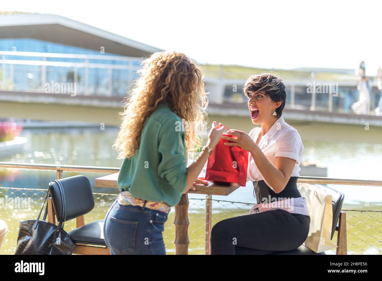 Deux femmes sur une terrasse extérieure.L'un d'eux est surpris et heureux de recevoir un cadeau de l'autre. Banque D'Images