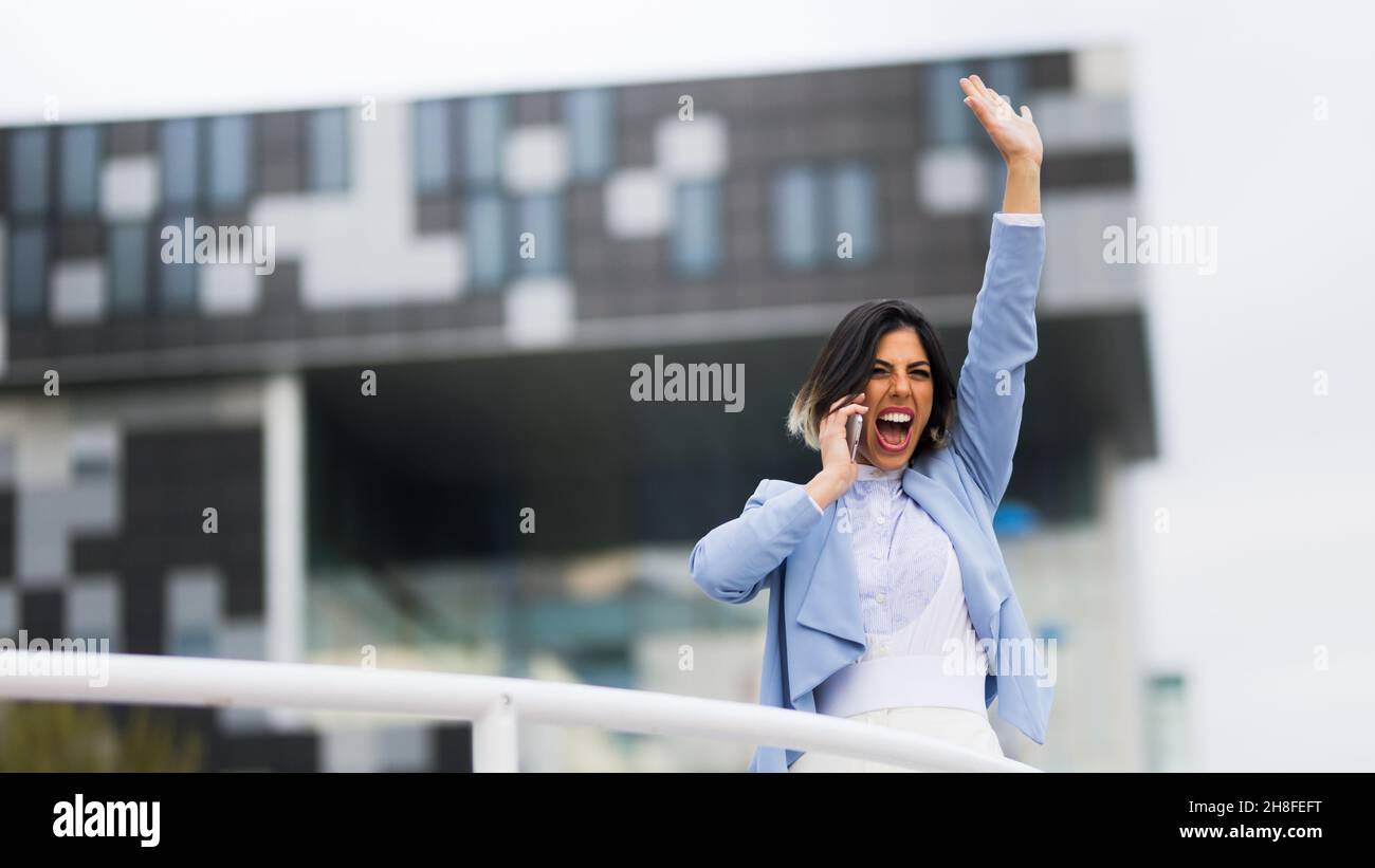Femme d'affaires réussie parlant sur son spartphone et célébrant avec joie Banque D'Images