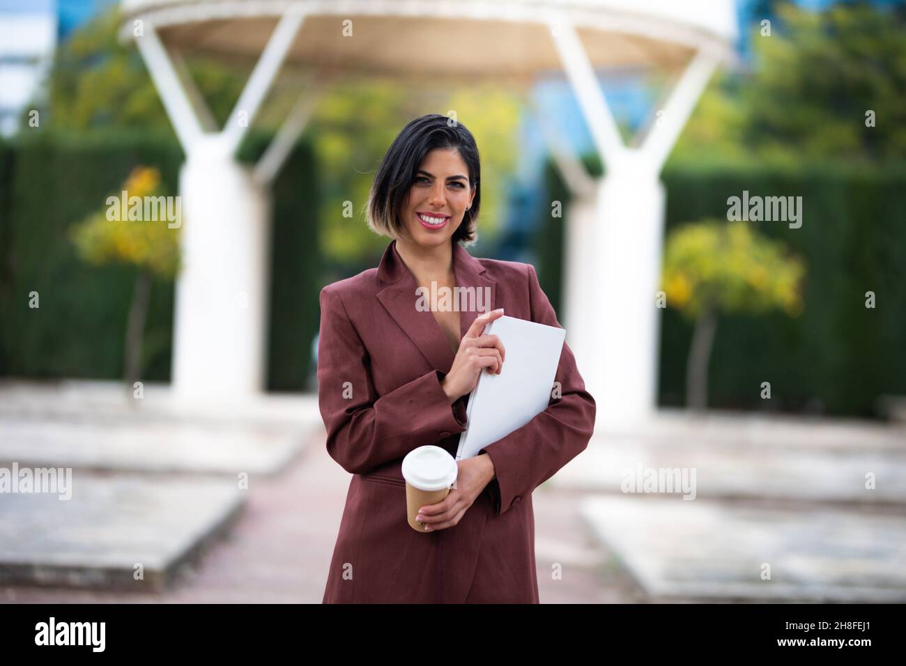 Portrait d'une femme d'affaires souriante avec un ordinateur portable et une tasse de café entre ses mains Banque D'Images
