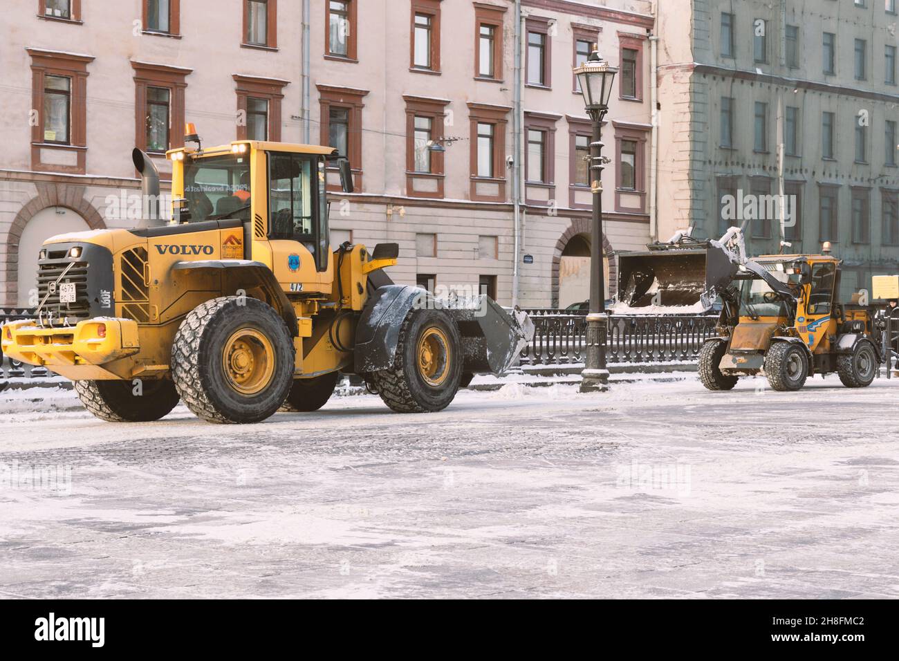 Saint-Pétersbourg, Russie - 16 janvier 2021: Le tracteur jaune Volvo et Wille défrichant la neige la rue dans le mauvais temps de proximité Banque D'Images