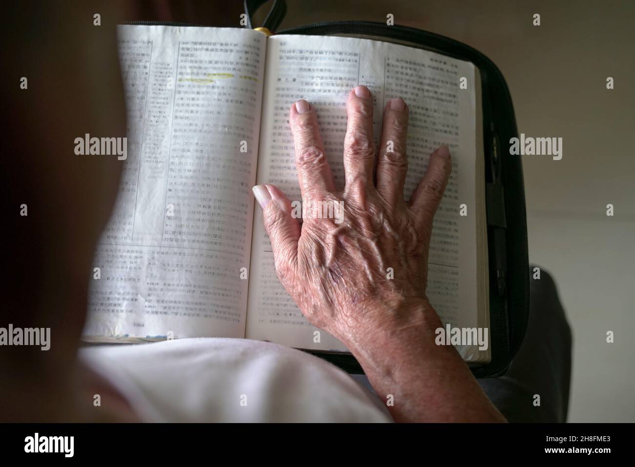 Main de l'homme senior au-dessus d'une Bible chinoise ouverte. Banque D'Images