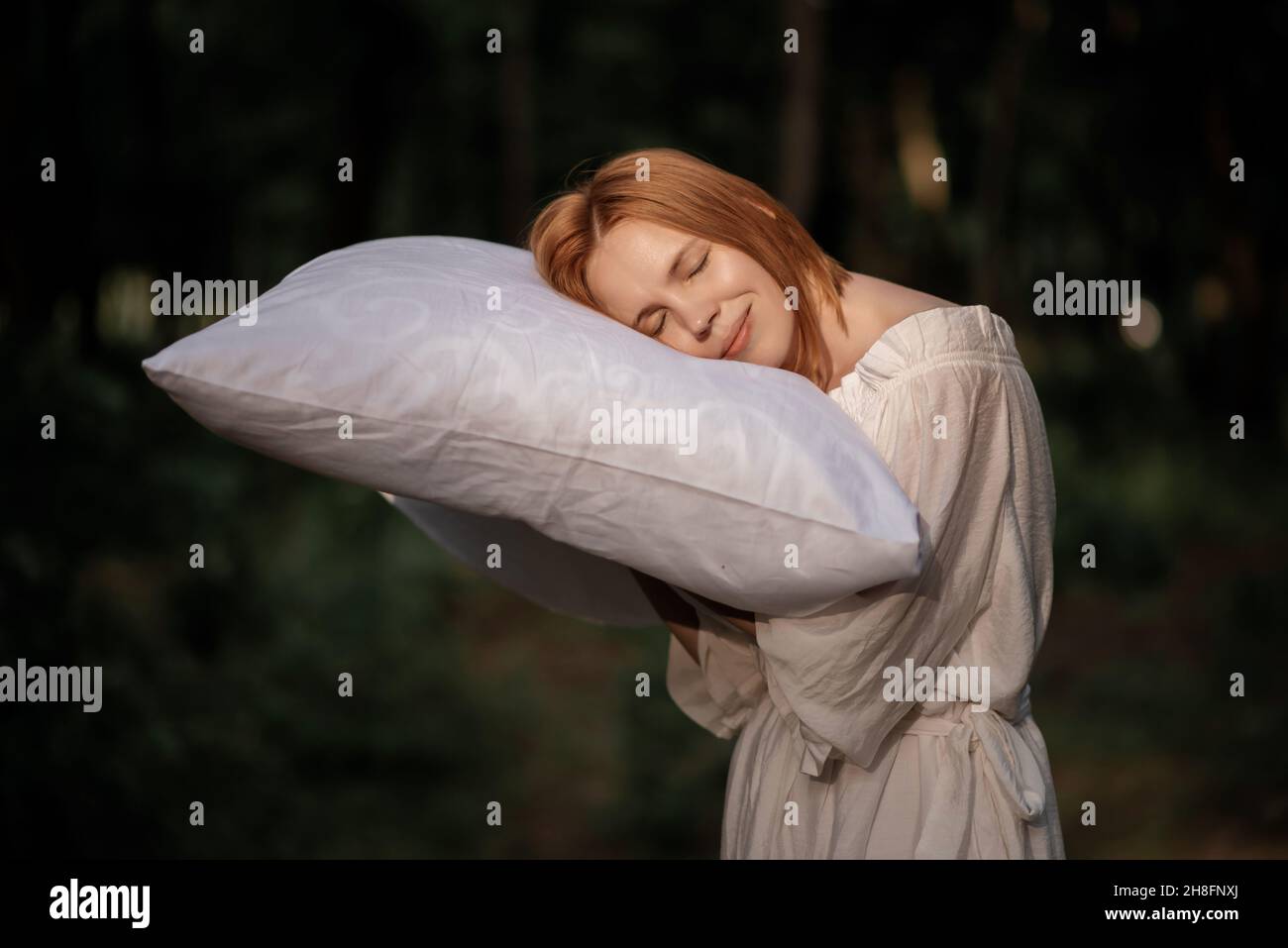 Une femme fatiguée et épuisée dort sur un oreiller qu'elle tient dans ses mains dans les bois.Désir de dormir, le temps mais le repos concept. Banque D'Images