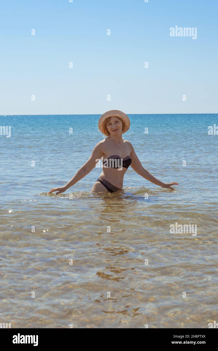 Une femme européenne en maillot de bain et en chapeau de taille dans la mer sourit et regarde dans la caméra.Vacances en bord de mer. Banque D'Images