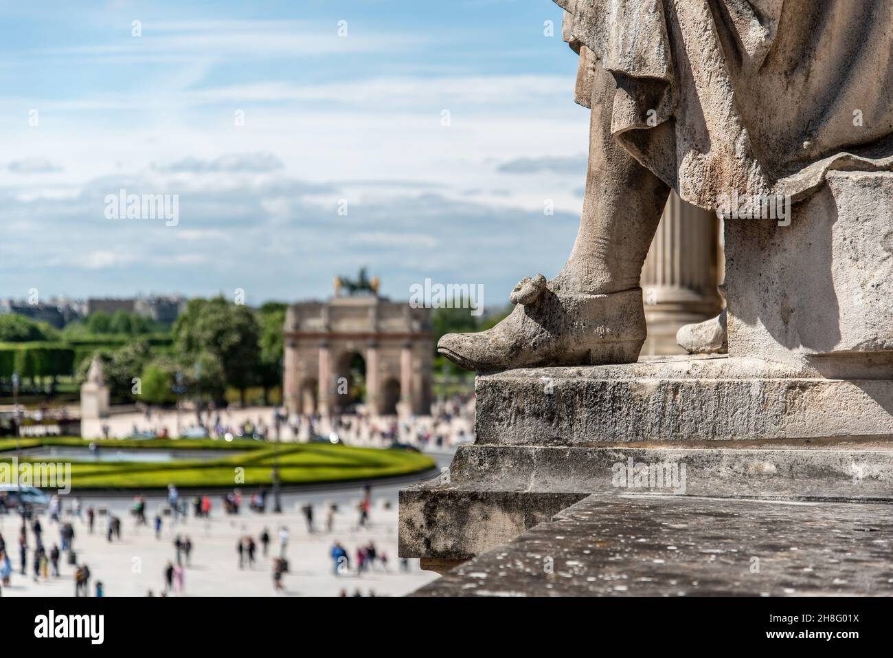 Le pied d'une statue sur le toit du Palais du Louvre avec une arche triomphale en arrière-plan, Paris, France Banque D'Images