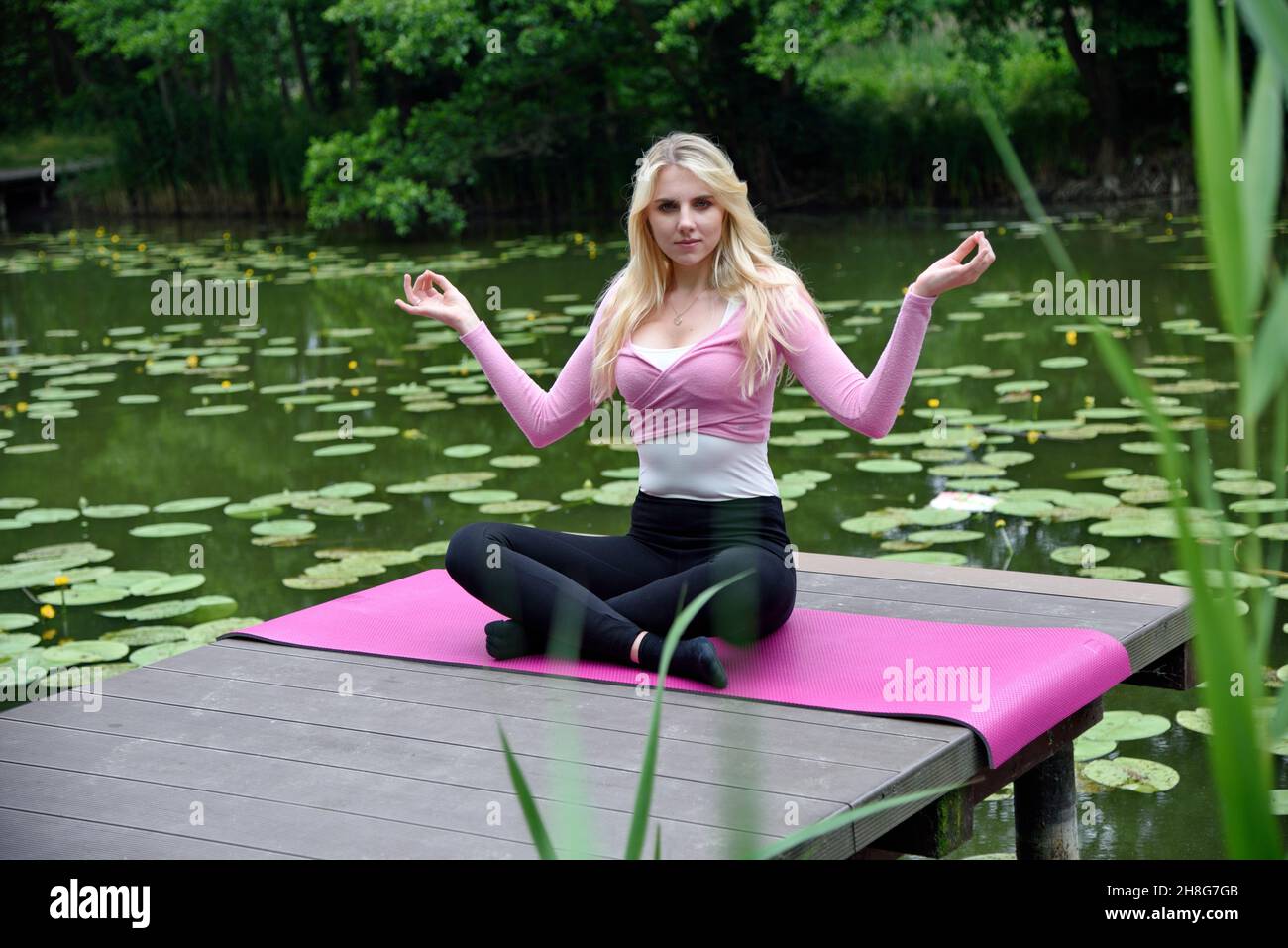 Jeune et mince femme s'exerçant dans le parc avec étang.Femme polonaise faisant un peu de yoga et d'étirement. Banque D'Images