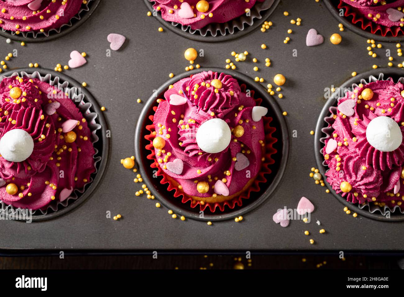 Délicieux petits gâteaux rouges à base de saupoudrés et de crème fouettée.Dessert rouge époustouflant avec des saupoudrés dorés. Banque D'Images