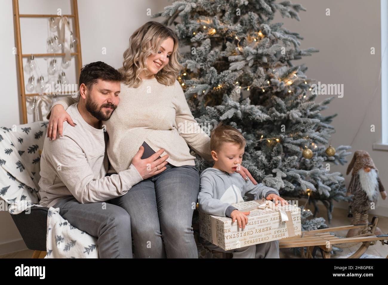 Bonheur de la famille de Noël Portrait de papa, mère enceinte et petit fils assis fauteuil à la maison près de l'arbre de Noël hug sourire européen jeune adulte f Banque D'Images