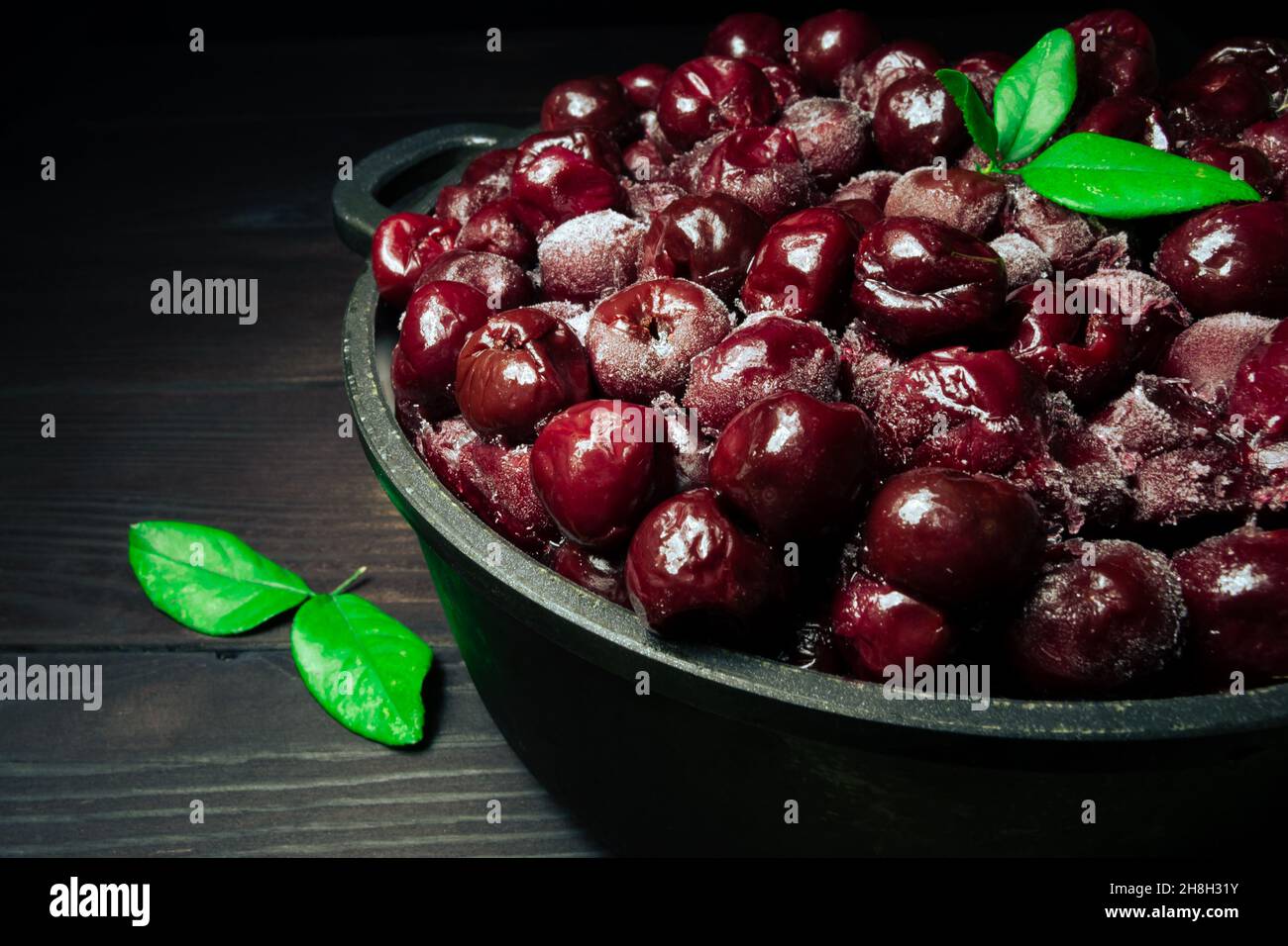 Beaucoup de cerise surgelée sans bâtons dans le bol avec des feuilles vertes sur un fond noir en bois.vitamines et une alimentation saine Banque D'Images