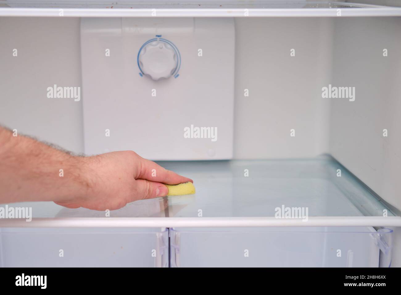Un homme main avec une éponge jaune lave le réfrigérateur Banque D'Images
