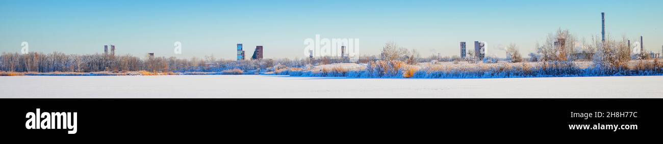 Une ancienne usine de produits chimiques abandonnée sur la rive d'une rivière d'hiver gelée recouverte de neige. Paysage industriel d'hiver Banque D'Images