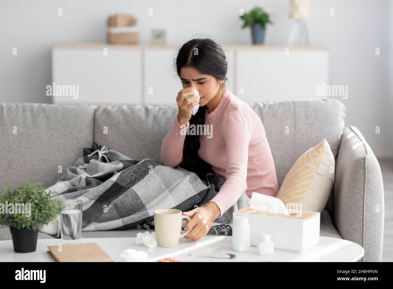 Contrarié triste millénaire femme indienne avec du plaid, souffrant de la grippe, le froid s'assoit sur le canapé, le nez de souffle dans la salle de séjour Banque D'Images